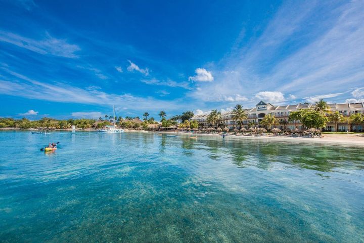 A person kayaking in crystal clear blue waters off Negri's 7 Mile Beach, with a beach resort behind them.