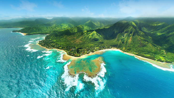 Ariel view of Kauai, Hawaii's mountainous region and a beautiful beach with clear blue waters.