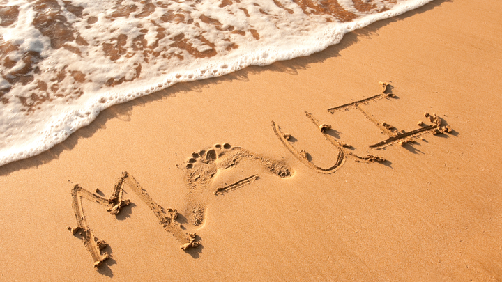 A beach in Maui, Hawaii with the word Maui written into the sand and water washing upon the beach.
