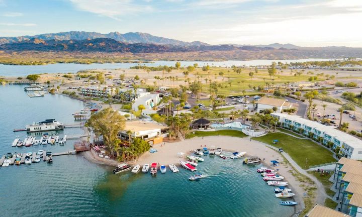 Aerial view of a popular swimming and boating area at Lake Havasu, Arizona, with sandy beaches, docked boats, waterfront resorts, palm trees, and mountains in the background.