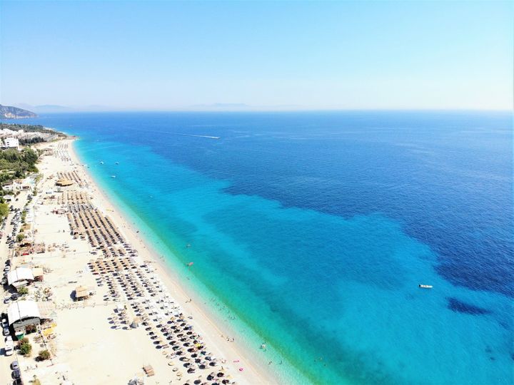 Ariel view of Plazhi i Dhërmiut Beach in Dhërmi, Albania with clear waters, beautiful clean sand and beach chairs. 