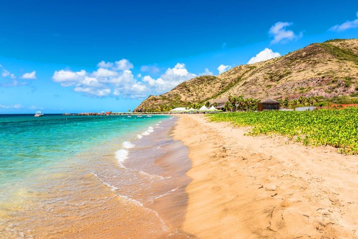 Clear blue waters washing on a sandy beach in St. Kitts with a mountain in the background.