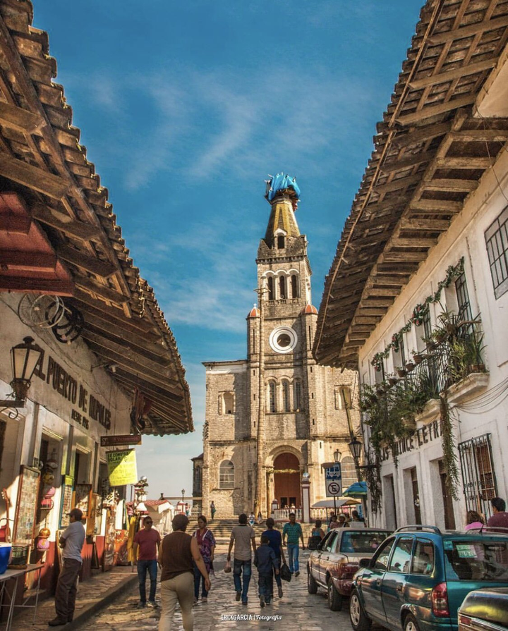 Cobblestone street in Cuetzalan del Progreso, Mexico, lined with colonial-style buildings and rustic wooden roofs.