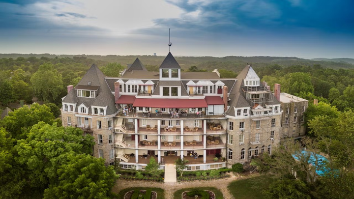Wide-angle aerial shot of the Crescent Hotel in Eureka Springs, Arkansas, showing Victorian architecture and forested surroundings at dusk.