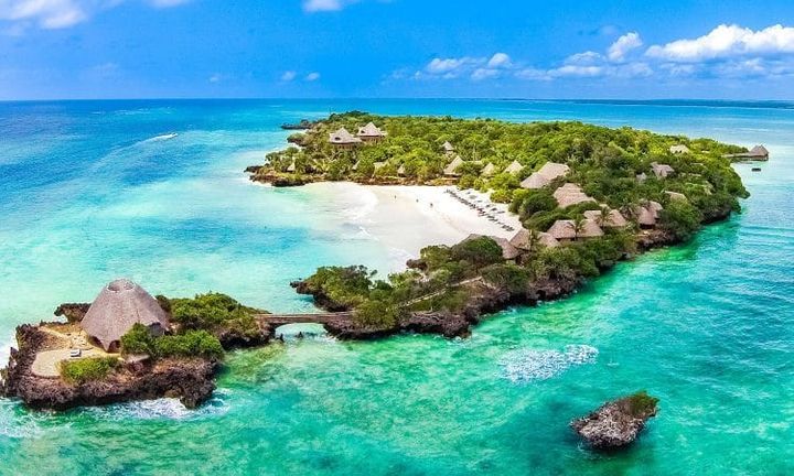 Funzi Island, Kenya, featuring lush green vegetation, traditional thatched-roof huts, and a beautiful beach with clear waters.