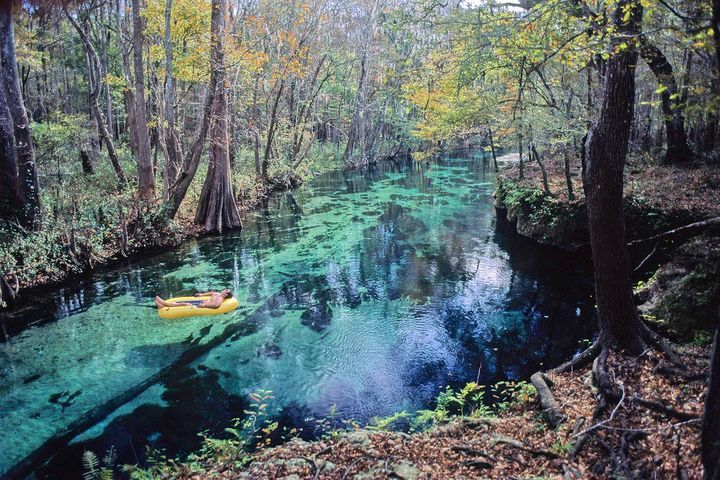 Person floating on a yellow raft in crystal clear waters surrounded by forest.  