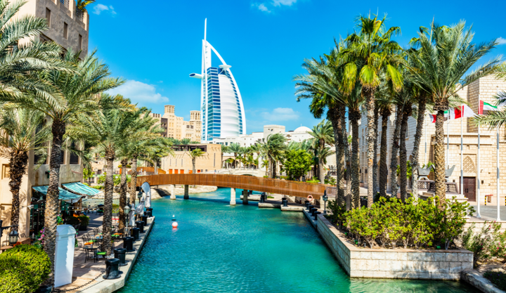 Jumeirah Burj Al Arab hotel in UAE seen at the end of a water way that is lined with palm trees in Dubai.