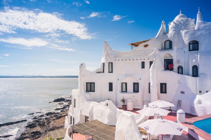The whitewashed, organic-shaped architecture of Casapueblo overlooks the Atlantic Ocean in Punta Ballena, Uruguay, under a bright blue sky.