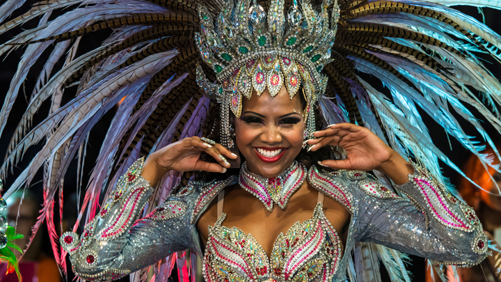 Smiling woman in an elaborate feathered costume and jeweled headdress during Carnival celebrations in Brazil.