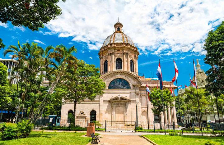 national pantheon of the heroes in Asuncion Paraguay with flags in front of it, and palm trees in the lawn.