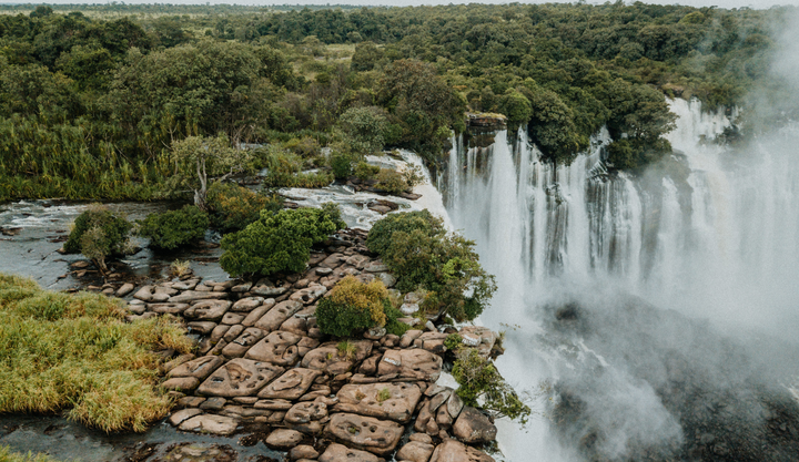 Aerial view of a lush green rainforest and rocky terrain surrounding Kalandula Falls in Angola.