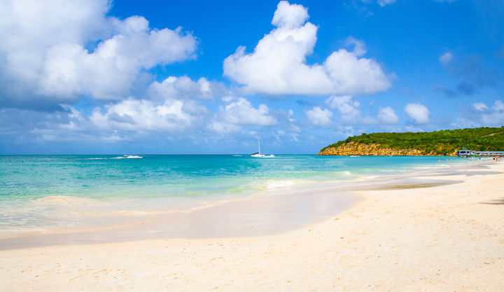 A beautiful beach in Antigua and Barbuda with sailboats anchored nearby.
