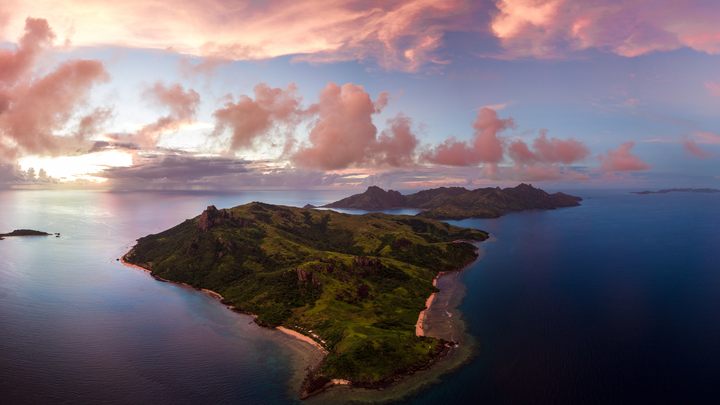 Ariel view of Yasawa Island, Fiji at sunset with clouds floating above the island, and calm ocean waters.