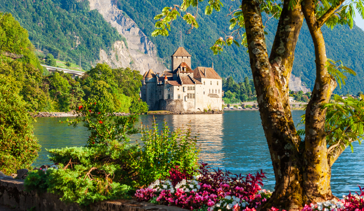 Chillon Castle in Switzerland in the summer time with bright colored flowers on the lakes edge.