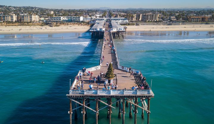 People enjoying the San Diego pier that sits high off the water with the beach in the backgrou