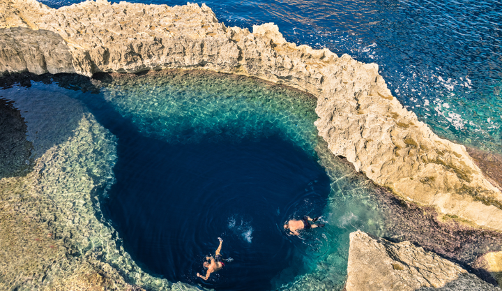 Swimming hole at Dwejra Bay (Gozo) Malta with two people swimming in a clear pool of water.
