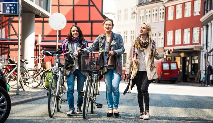 Three girls walking with bicycles in the streets of Copenhagen, Denmark. 