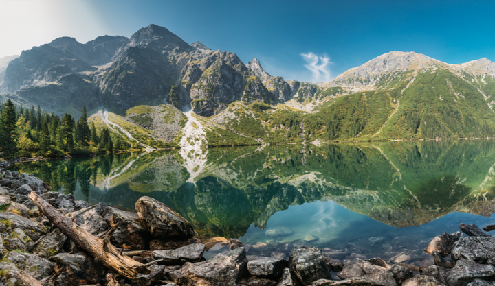 A beautiful lake under clear blue skies with mountains in the background at Tatra National Park in Poland.