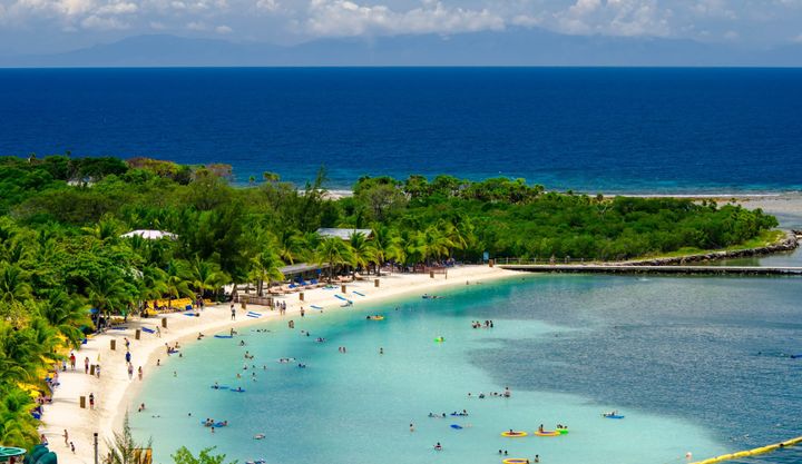 People playing on a beautiful beach with clear blue waters at Mahogany Bay beach resort, Honduras