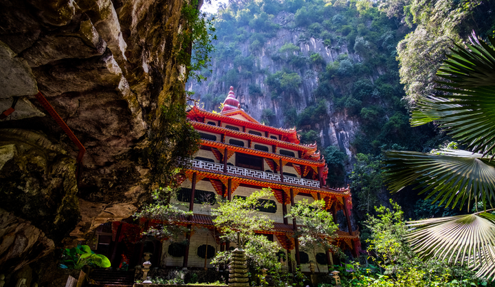 Temple caves in Malaysia in front of a mountain and surrounded by jungle.