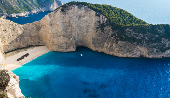 Ariel view of a beach surrounded by tall rock clffs with a shipwreck on the beach at Navagio Beach.