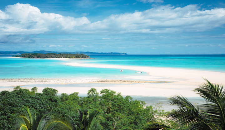 A panoramic view of Nosy Iranja Island in Madagascar, featuring a long white sandbar connecting two lush green islets surrounded by vibrant turquoise waters.