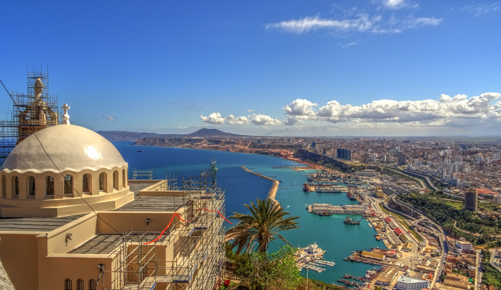 Ariel view of the city of Oran, Algeria sitting on the ocean front with a few clouds in the sky.
