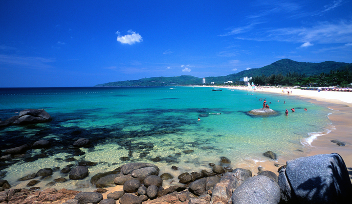 View of Kata Beach in Phuket, Thailand, with turquoise water, rocky shore, and people swimming.
