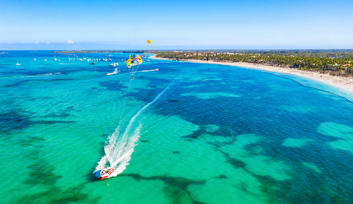 Ariel view of a small boat moving through clear blue waters near the beach in Punta Cana.