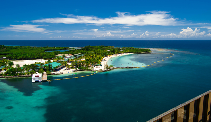 Looking off an a balcony at a beautiful beach with people swimming in Roatán Island, Honduras. 
