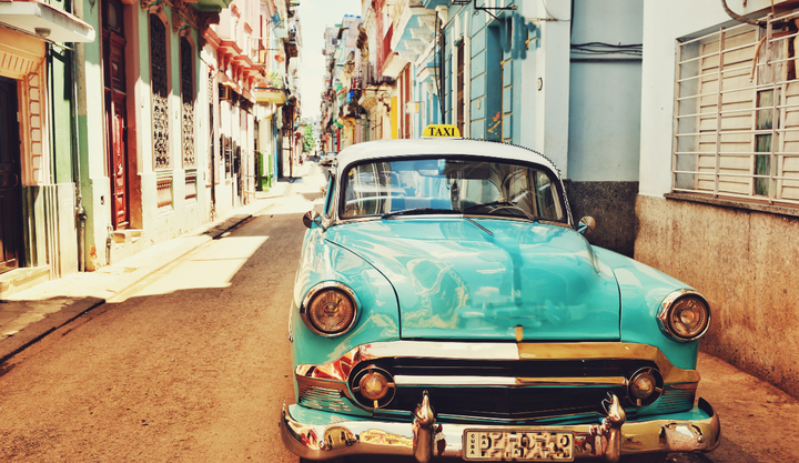 A blue vintage car in the streets of Havana Cuba parked in the street between two buildings.