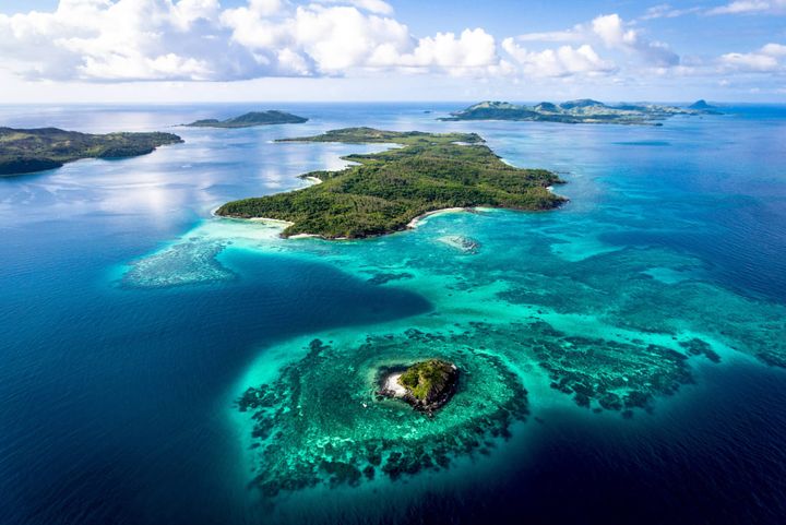 Ariel view of islands in Fiji with pretty blue clear waters surrounding them.