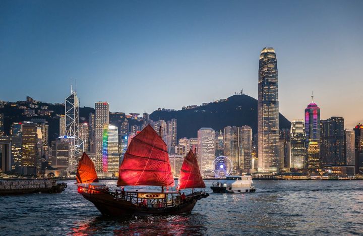 A chinese style sailboat with red sails in Hong Kong with the skyline in the background at night.