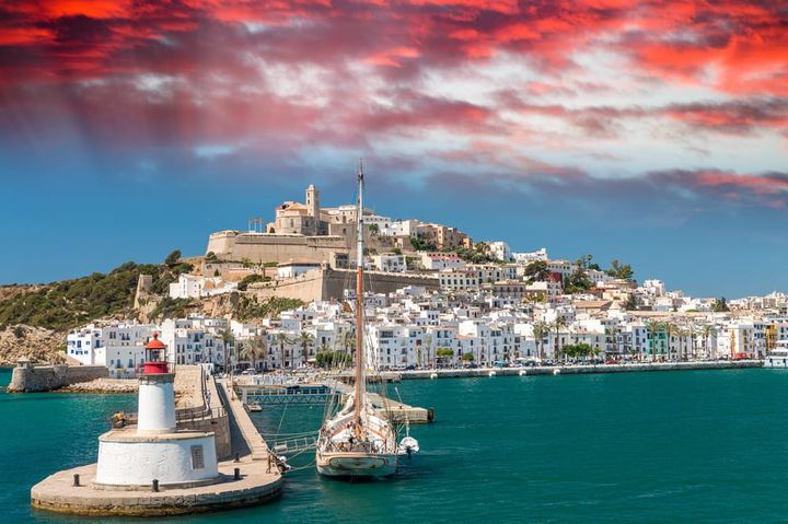 Boat anchored at a pier in Ibiza, Spain near sunset with resorts seen in the background.