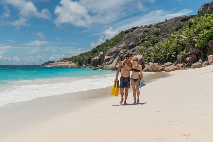Two people walking on the beach in Seychelles with snorkel equipment.