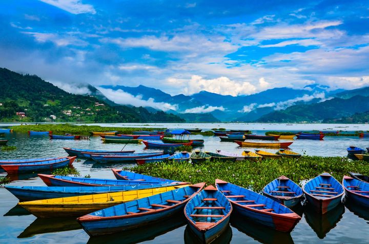 Blue canoes on a lake with mountains in the background in Nepal.