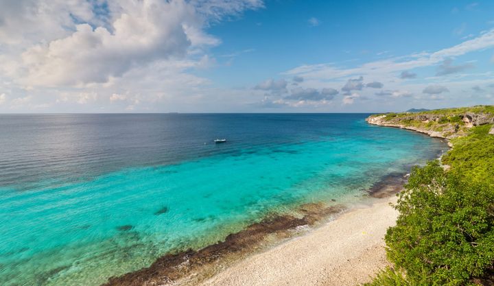 A beautiful beach in Bonaire, with a boat anchored in clear blue waters nears the beach.