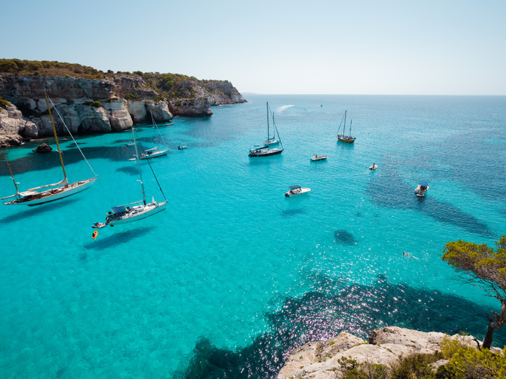 Sailboats anchored in clear blue waters on the coast of Menorca.