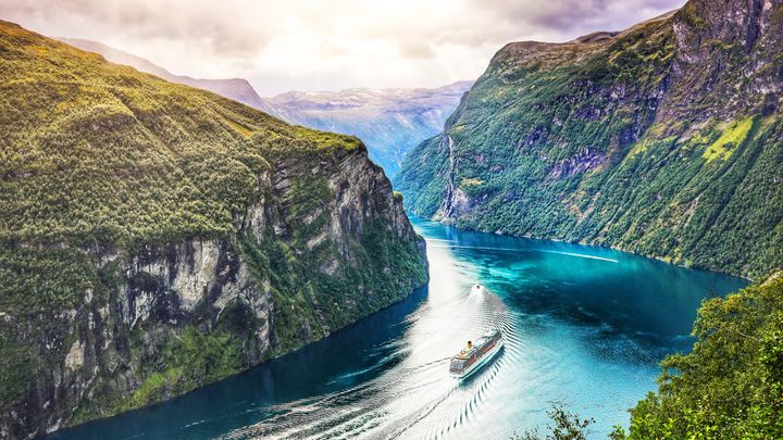 A fjord in Norway in the summer time with a cruise ship going through the fjord. 