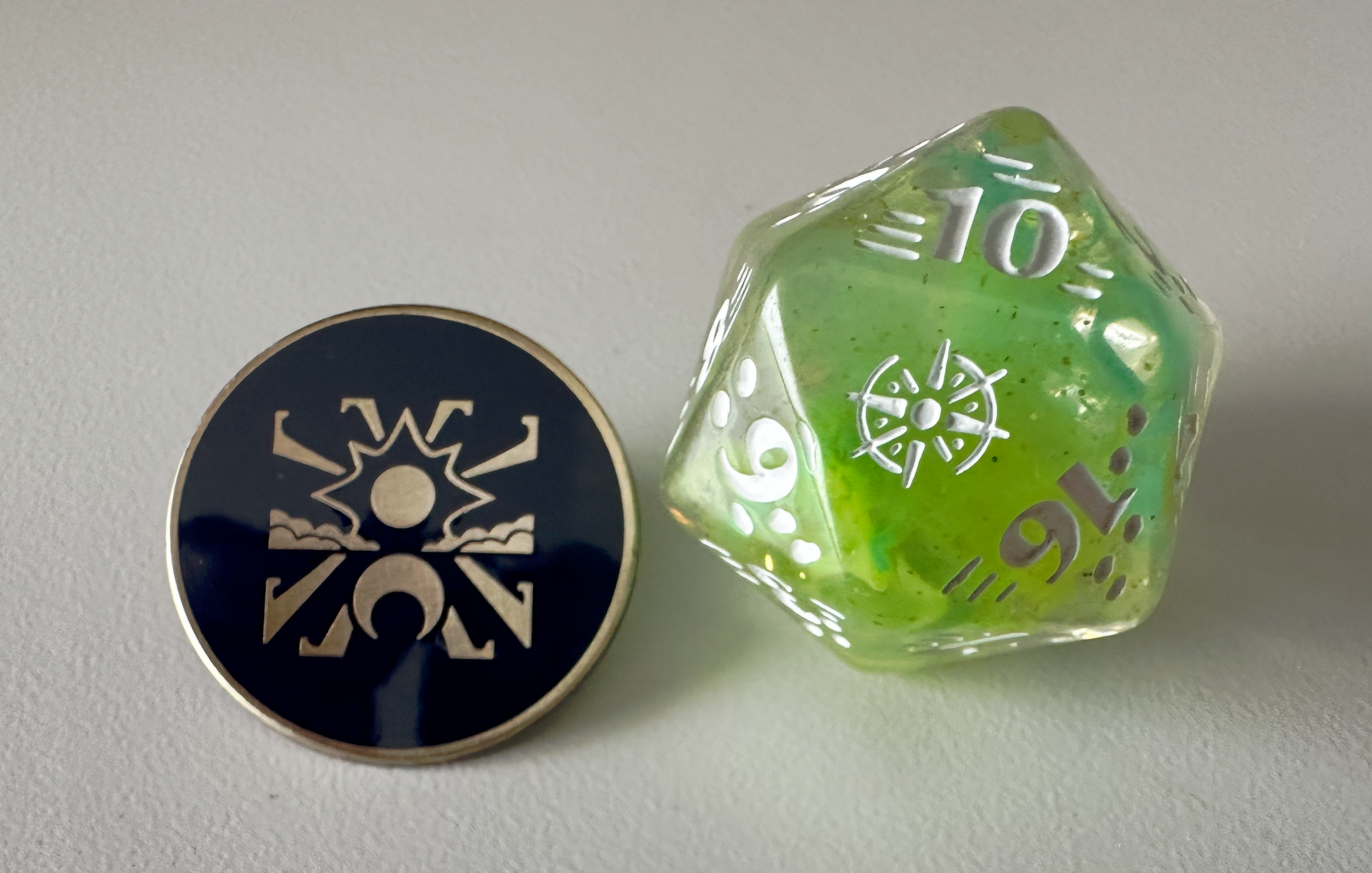 A pin with a symbol on it and green chunky dice with the Wardens logo for the 20