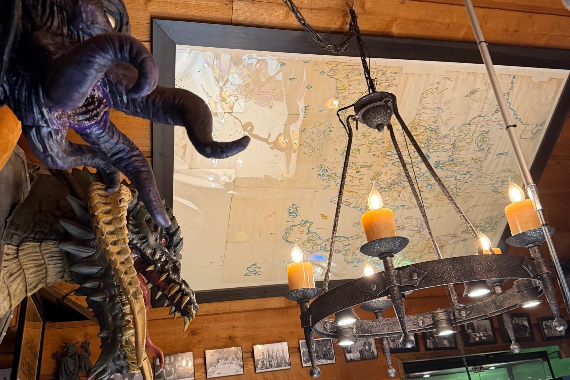 A sloped wooden ceiling holds Ed Greenwood's original handdrawn map of the forgotten realms in a frame. A mind flayer and a dragon head is visible to the left and a gothic chandelier hangs in the center.