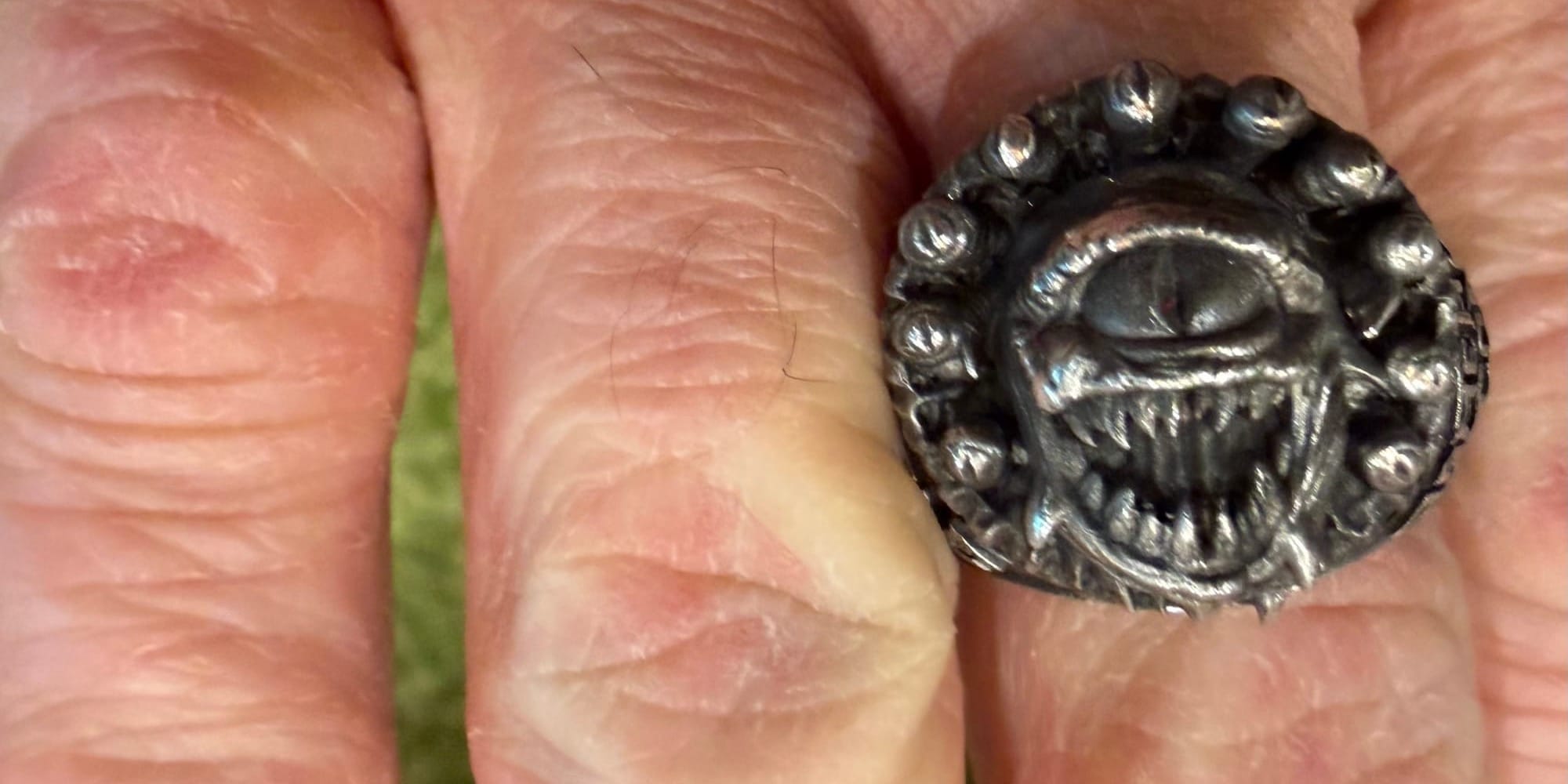A beholder ring. Many eyes around the single eye and a wide mouth of teeth. My embarrassingly dry fingers are also in the picture.