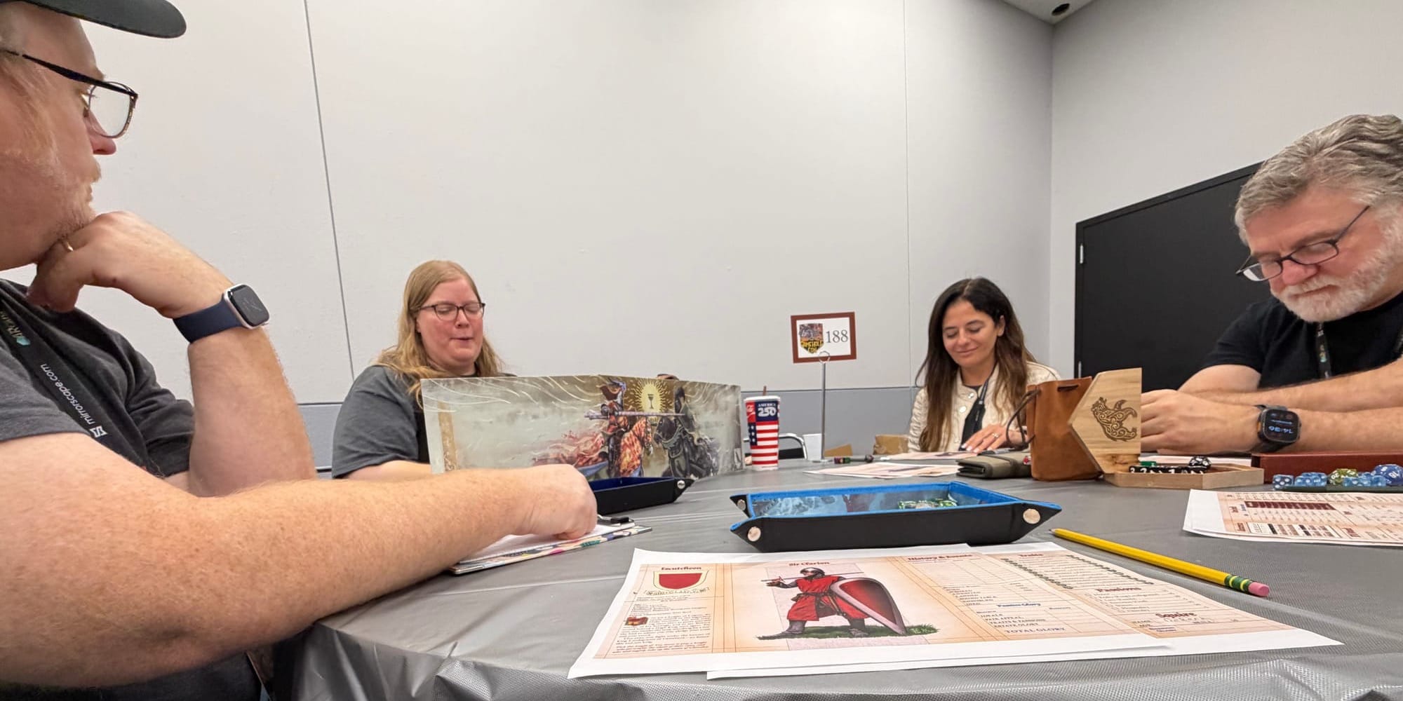 Four people sitting at a table playing Pendragon. My character sheet is in the foreground and the GM is behind a colorful screen.