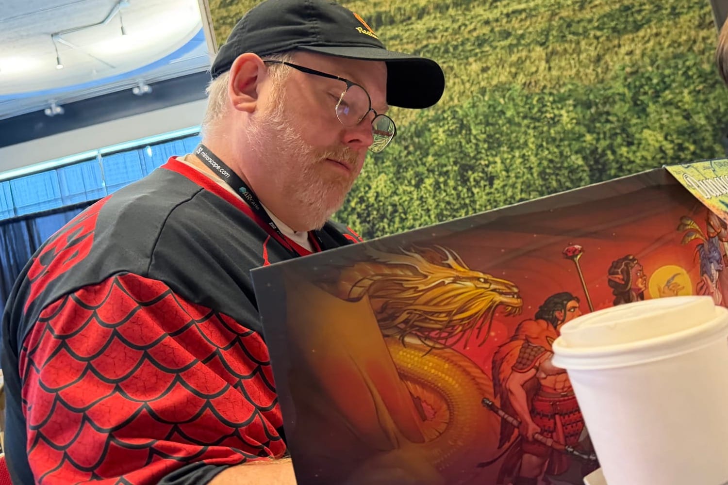 Eric Menge in baseball cap and red dragon scaled shirt behind his DM screen.