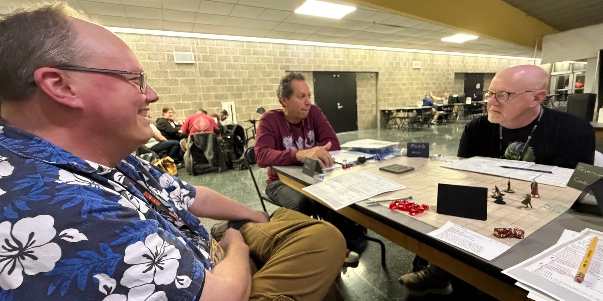 A table in the open gaming area, with two of the players to either side of the GM. Dice and tokens on the table.