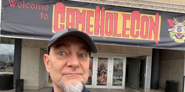 Lou in front of the convention center beneath a big banner that says Welcome to GameHole Con