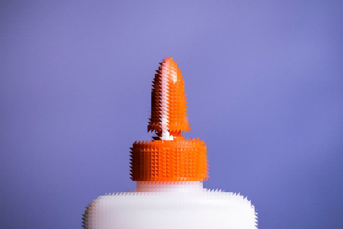 Picture of the top of a glue bottle.  Orange tip. White body.  Tip is open. There is a bead of glue running down the tip.