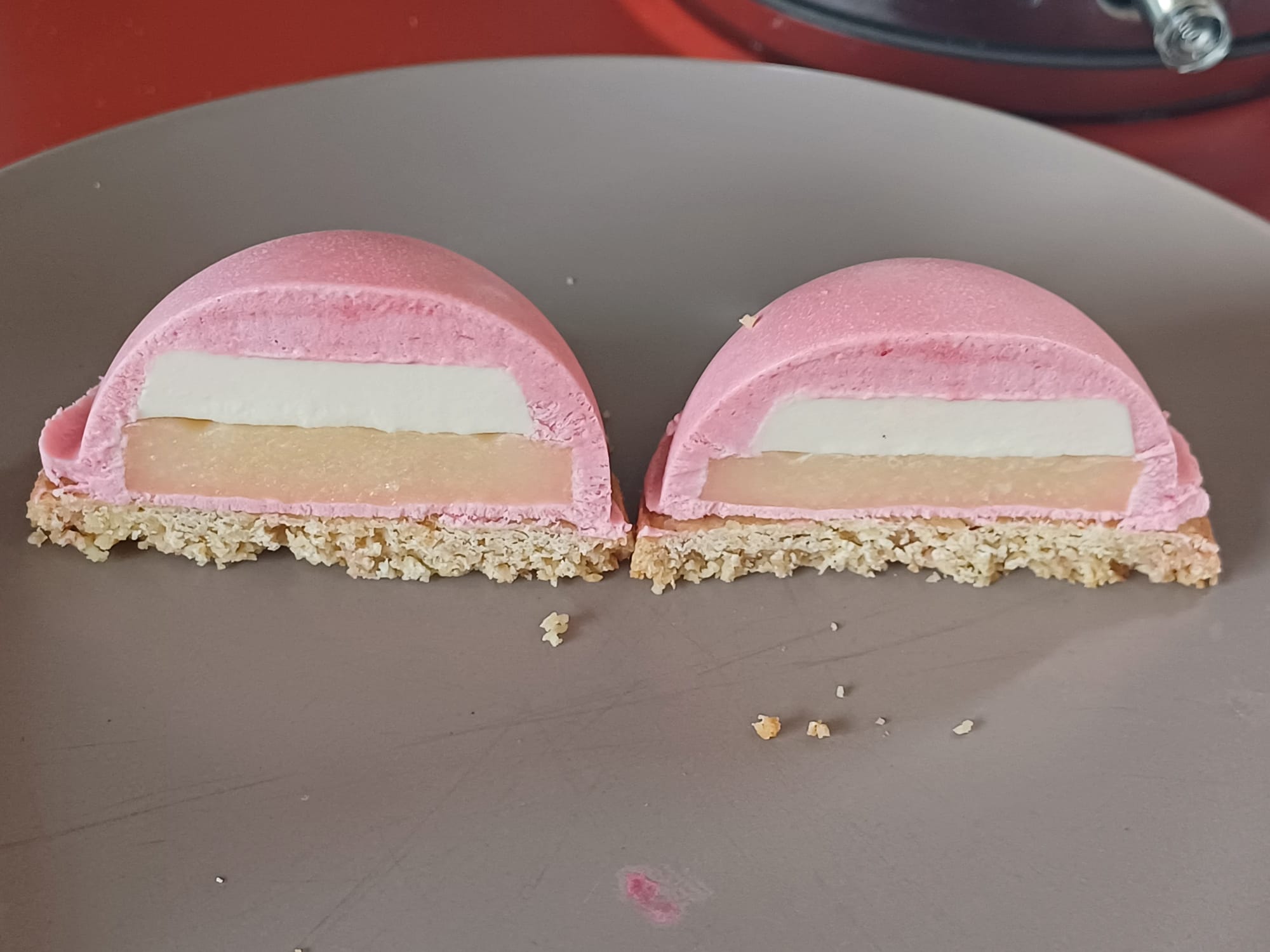 ENTREMET. A dome, cut in half, showing a pink raspberry mousse, coconut milk panna cotta, lemon curd gelee, and shortbread base
