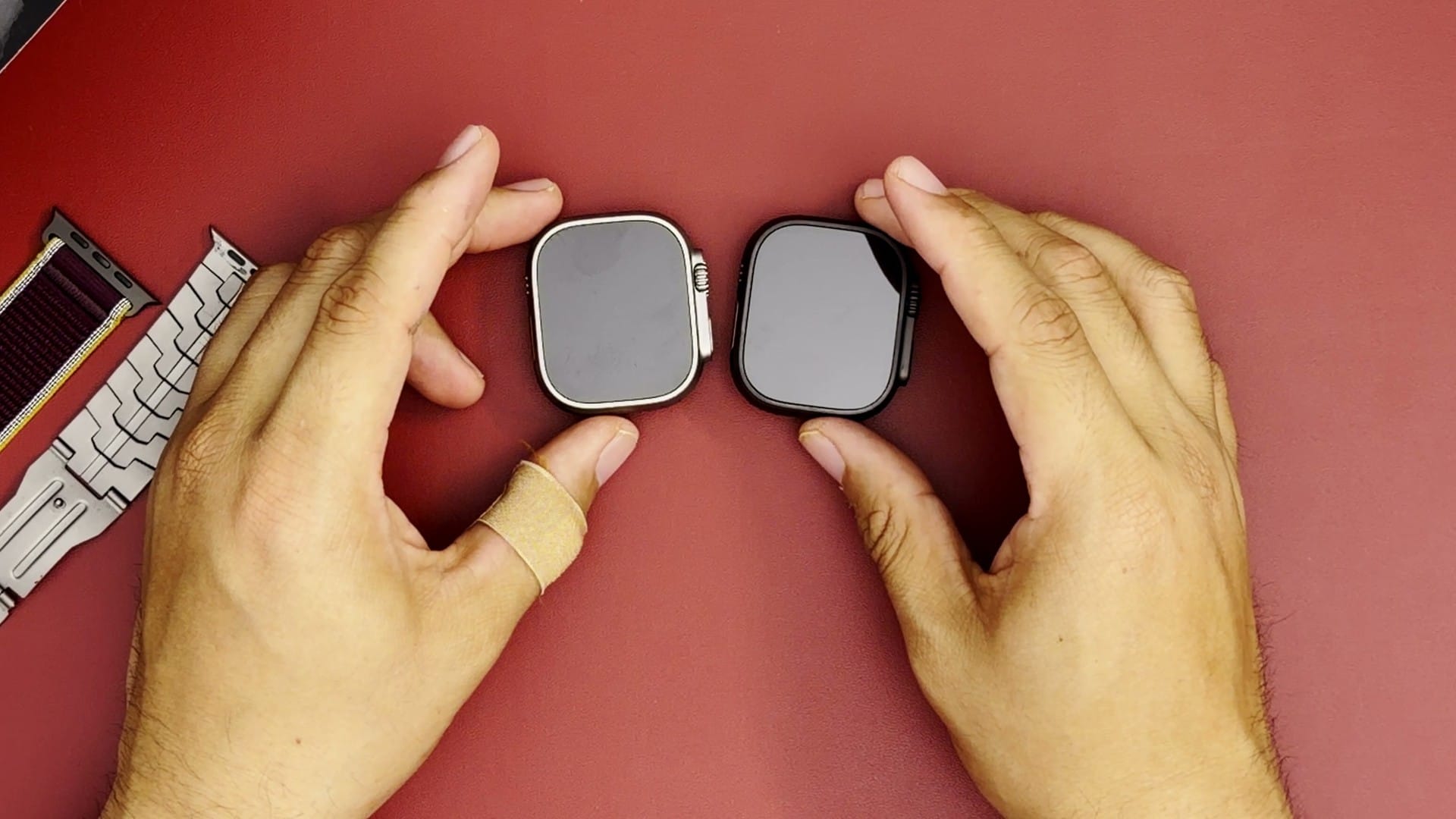 Apple Watch Ultra 2 in natural titanium and Ultra 4 in black titanium face up on a red mat