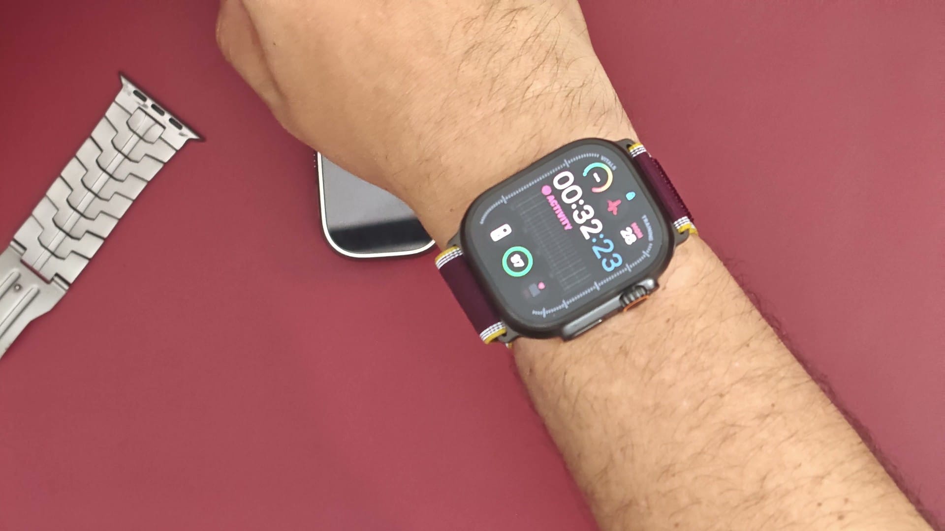 Black titanium Apple Watch Ultra 4 with a burgundy band on a wrist, watch face lit